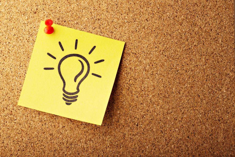 Picture of a post it note tacked to a corkboard with a light bulb drawn on it.