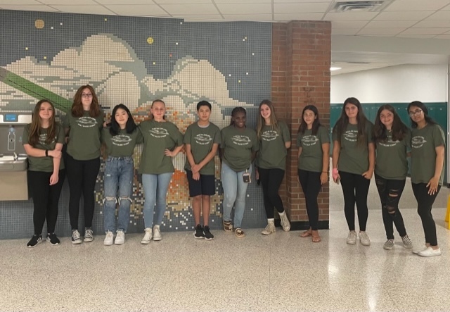 Picture of students wearing logo t-shirts against a brick wall and a hall way.